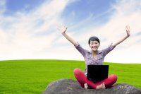 Young woman with laptop outside with arms raised