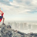 Individual in super hero cap standing on top of a mountain